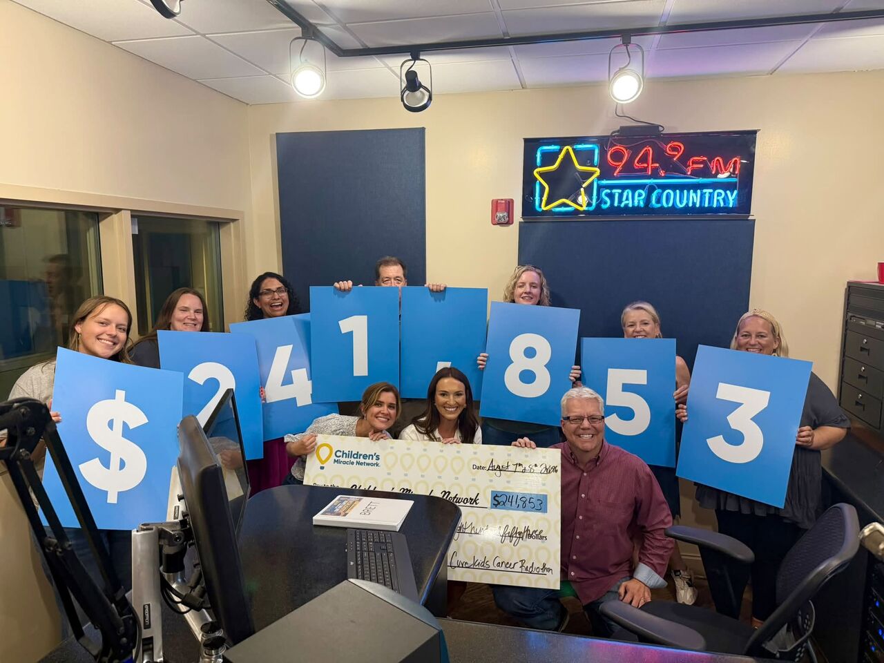 Staff holding up numbers for the amount of money raised during the Radiothon