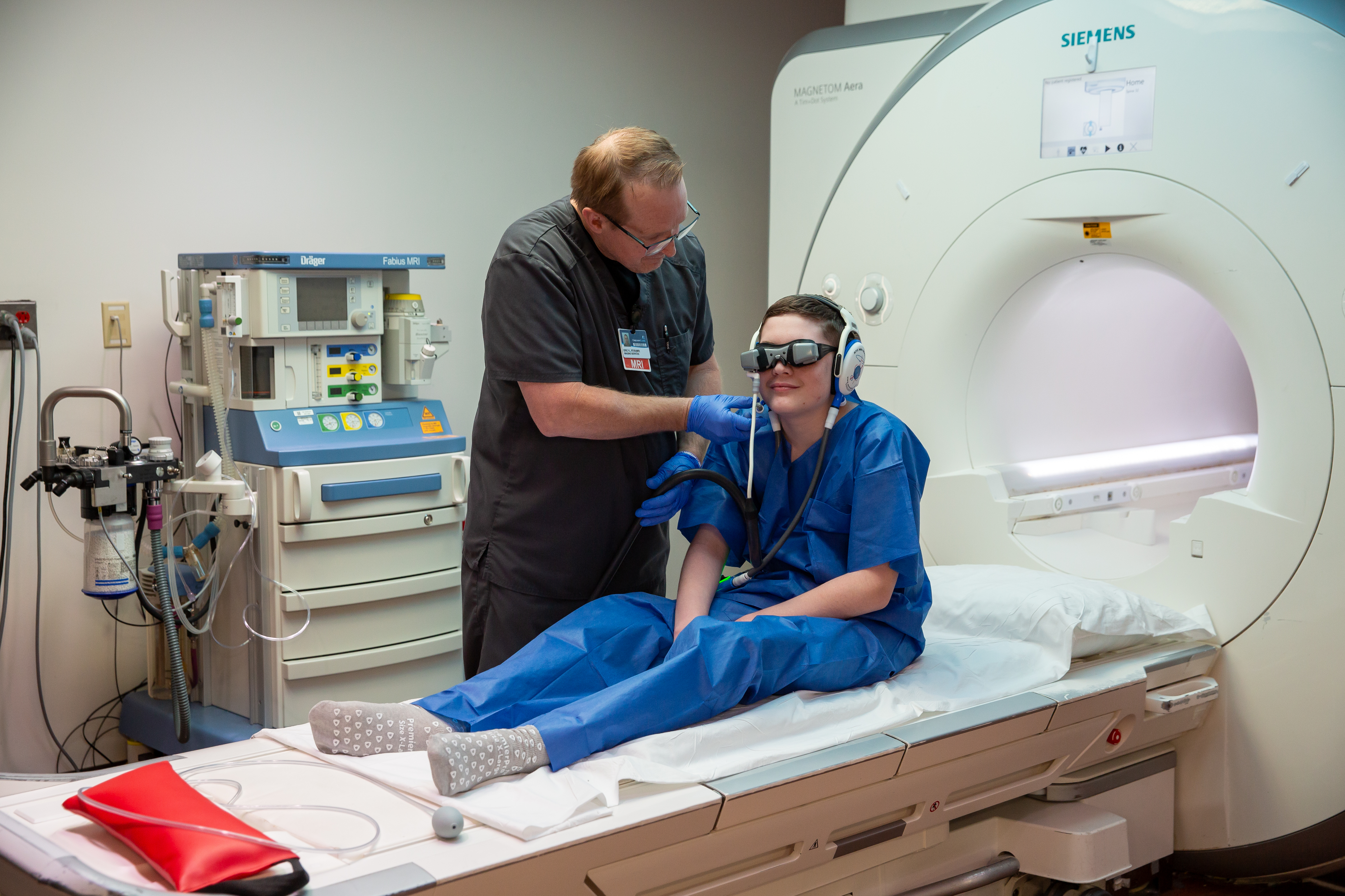 When 13-year-old Elias Dalton recently slid into the Magnetic Resonance Imaging (MRI) machine at Carilion Clinic, for once, he was not anxious about the noise, tight space or staying still. Instead, he was focused on watching Marvel movies through a pair of specialized CinemaVision goggles.  For Elias Dalton, who has tuberous sclerosis and autism, that experience marked a significant change. Since age five, he has required regular MRIs—procedures that often required sedation because remaining still for long scans can often be difficult.  “He never enjoyed going under anesthesia, and always felt terrible coming out of it,” said Adam Dalton, Elias’ father. “One time he even woke up and didn’t remember his mom or me, and it took a while for his memory to come back. That was the last time he went under.” Now, thanks to two pairs of CinemaVision MRI goggles, funded through grants from Child’s Play Charity, the Foster Family Foundation, and an anonymous donor, children like Elias can watch movies during their scans—often eliminating the need for anesthesia. MRIs require patients to lie completely still for extended periods, which can be especially challenging for children. Traditionally, sedation has been used to help but requires additional coordination and recovery time and carries potential risks.  The goggles, purchased for Carilion Children’s Child Life Program, allow pediatric patients to watch movies or shows safely inside the machine, helping children relax and stay still naturally.  Donated funds also helped build a library of more than 100 DVDs, giving children a wide selection of movies to choose from during their scans. “Our goal is always to provide the most comfortable experiences for our patients, especially our pediatric patients,” said Teresa Crowder, Imaging Manager at Carilion. “If we can help a child successfully complete an MRI without anesthesia, that’s even better.” Like they did for Elias, these goggles have helped more than 50 young patients get through MRIs without having to undergo anesthesia. By reducing the need for anesthesia, the goggles help avoid potential medication complications and may shorten scheduling wait times for MRI appointments. As a not-for-profit health system, Carilion relies on grants and donations from organizations such as Child’s Play Charity, the Foster Family Foundation, and community to help provide the very best care and comforts for Carilion’s patients, staff, and community. 